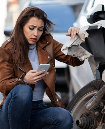 Kraschad bil med kvinna intill som håller i telefon